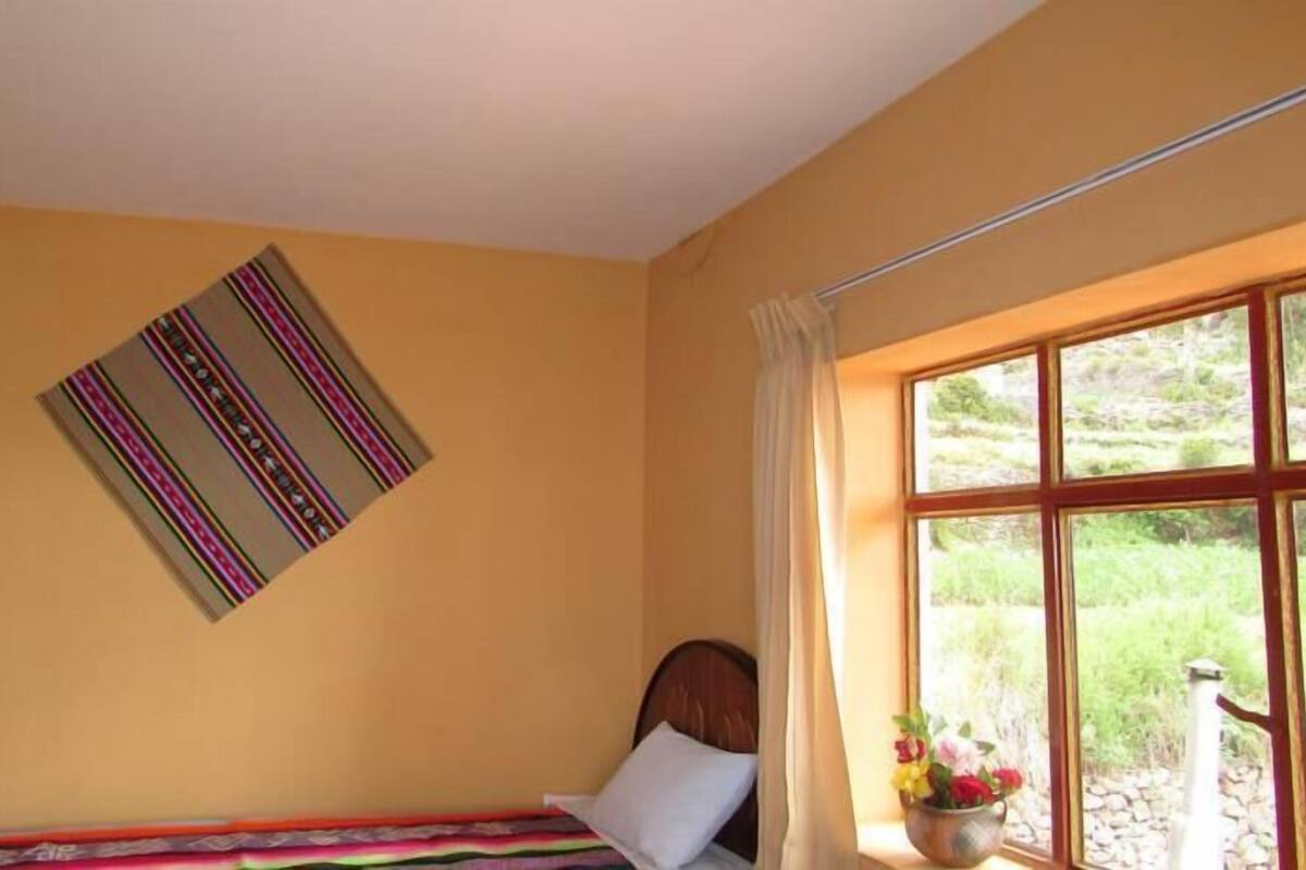 A room with a bed, a window with curtains, and a wall-mounted artwork.