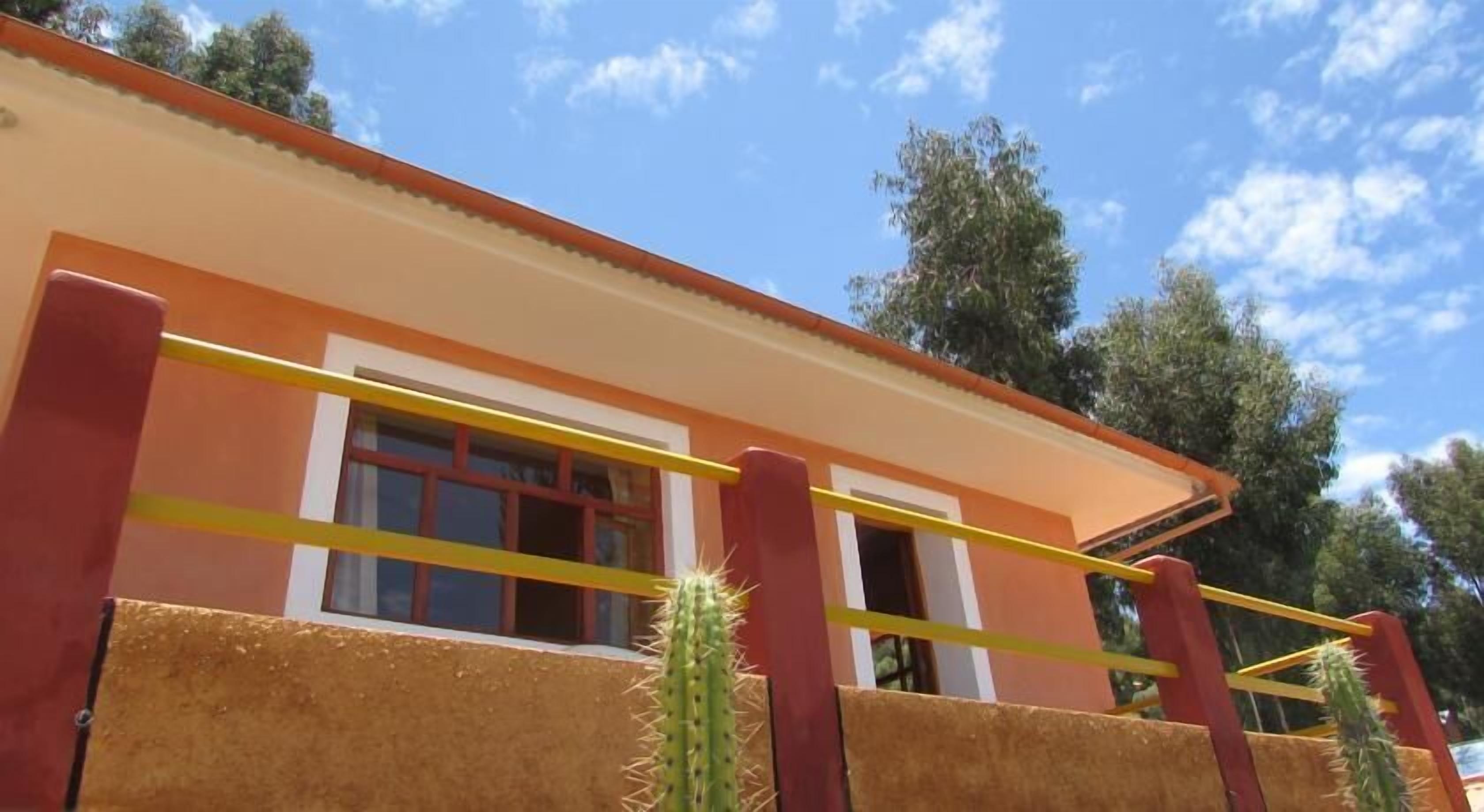 A building with a red and yellow exterior, a window with a yellow frame, and a cactus in front.