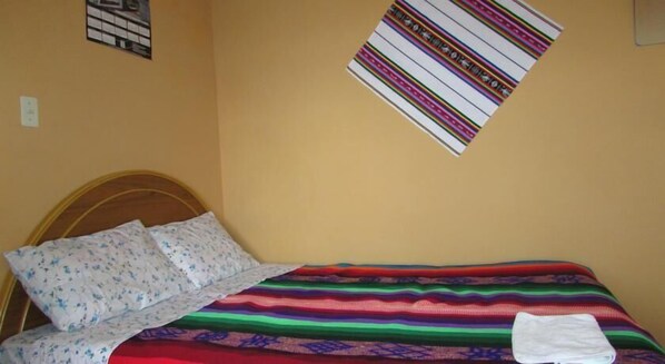 A bed with a colorful striped blanket and floral pillows, a wooden headboard, and a wall-mounted striped artwork.