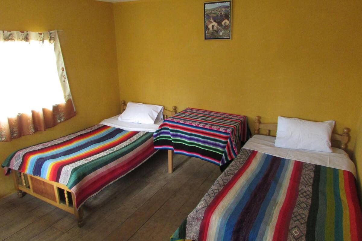 A room with two single beds, each with a colorful striped blanket, wooden headboards, and white pillows.