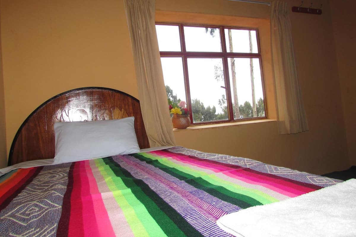 A bed with a colorful striped blanket, a wooden headboard, and a window with curtains.