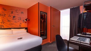 A hotel room with a bed, a desk with a laptop, a coat rack, and a door leading to a closet. - Ibis Styles Paris Gare de l'Est Magenta (Paris)
