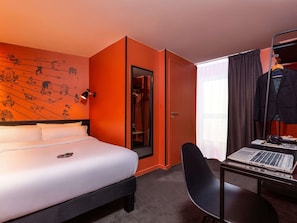 Una habitación de hotel con una cama, un escritorio con una computadora portátil, un perchero y una puerta que da a un armario.