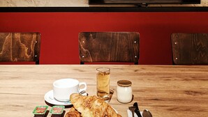 Un comedor con mesa de madera, sillas, televisor montado en la pared y una pared roja.