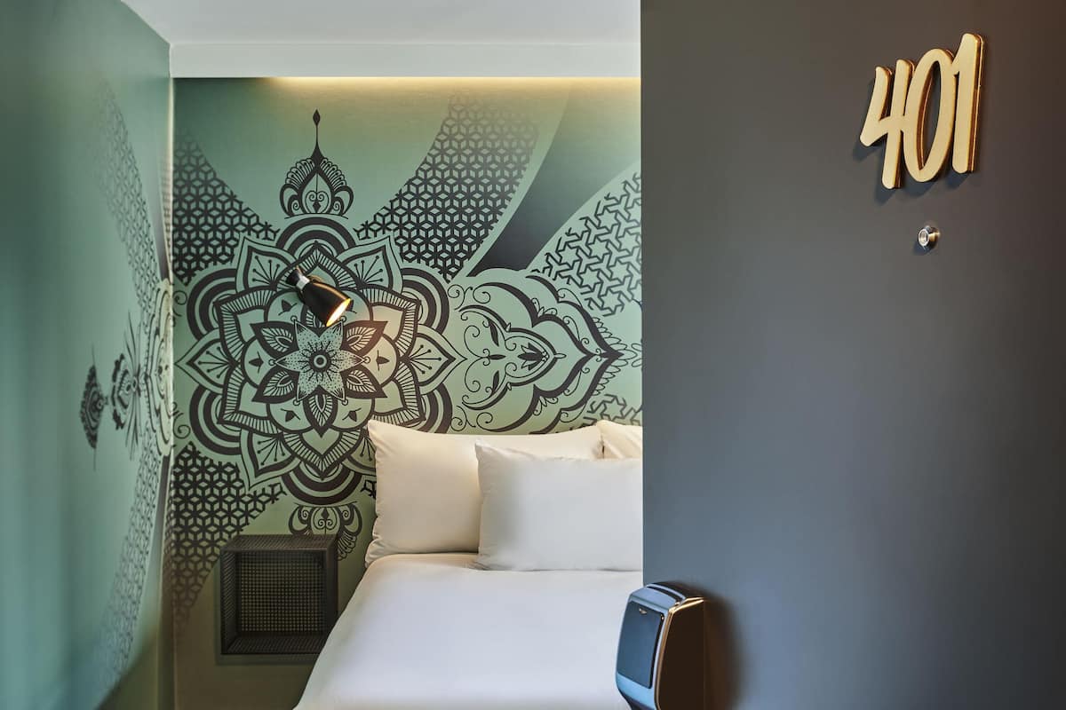 Une chambre d’hôtel avec un lit, une lampe fixée au mur et un motif décoratif sur le mur.