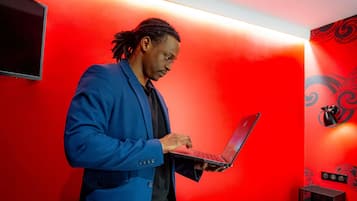 A person in a blue coat using a laptop in a room with red walls and a black and red decorative panel.