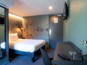 Habitación de hotel con cama, mesita de noche, control remoto y un vaso de agua.