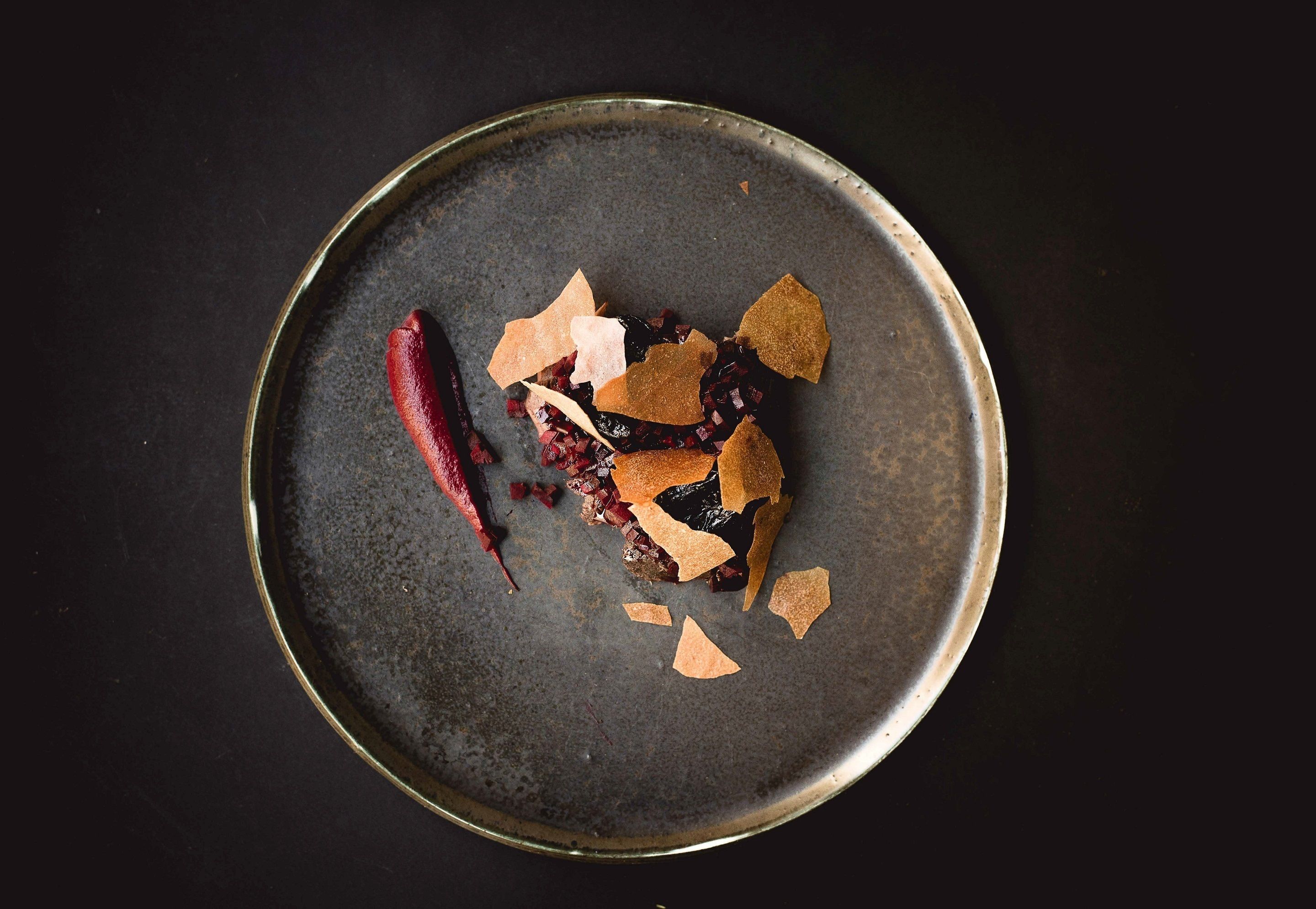 Un plato redondo y oscuro con algunos alimentos y un chile rojo sobre una superficie negra.