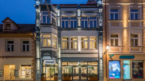 Un hotel de estilo arquitectónico europeo tradicional, con entrada en esquina, ventanas grandes y un restaurante visible en la planta baja llamado "Artagnost".