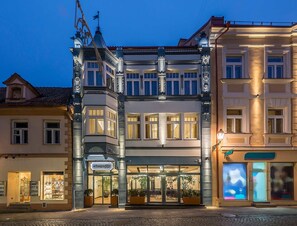 Un hotel de estilo arquitectónico europeo tradicional, con entrada en esquina, ventanas grandes y un restaurante visible en la planta baja llamado "Artagnost".