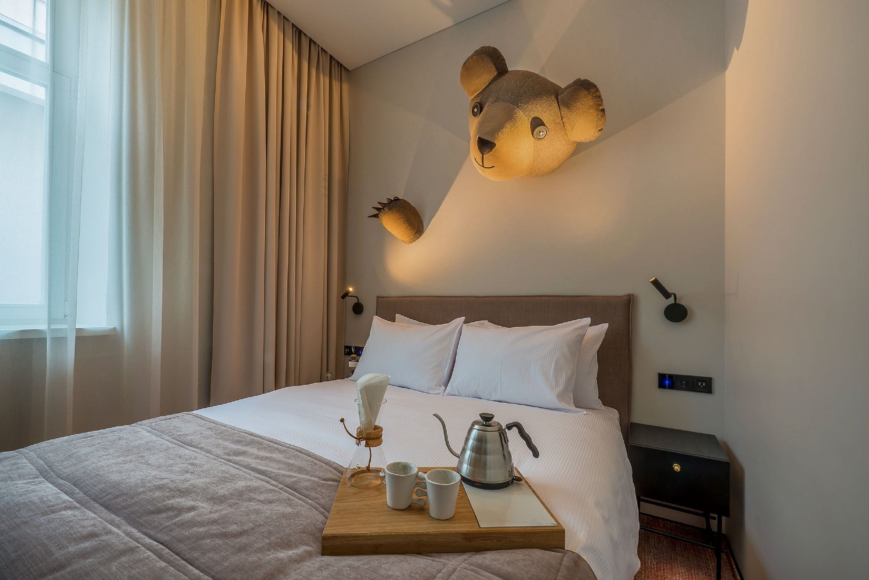 A neatly made bed with a tray of coffee and cups, a bear-shaped light fixture, and a nightstand with a lamp.