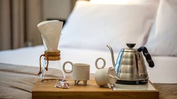 Una bandeja de madera con una cafetera, dos tazas y un recipiente de vidrio sobre una cama.