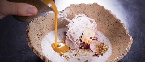 A hand pouring a sauce into a bowl containing a salad with various ingredients.