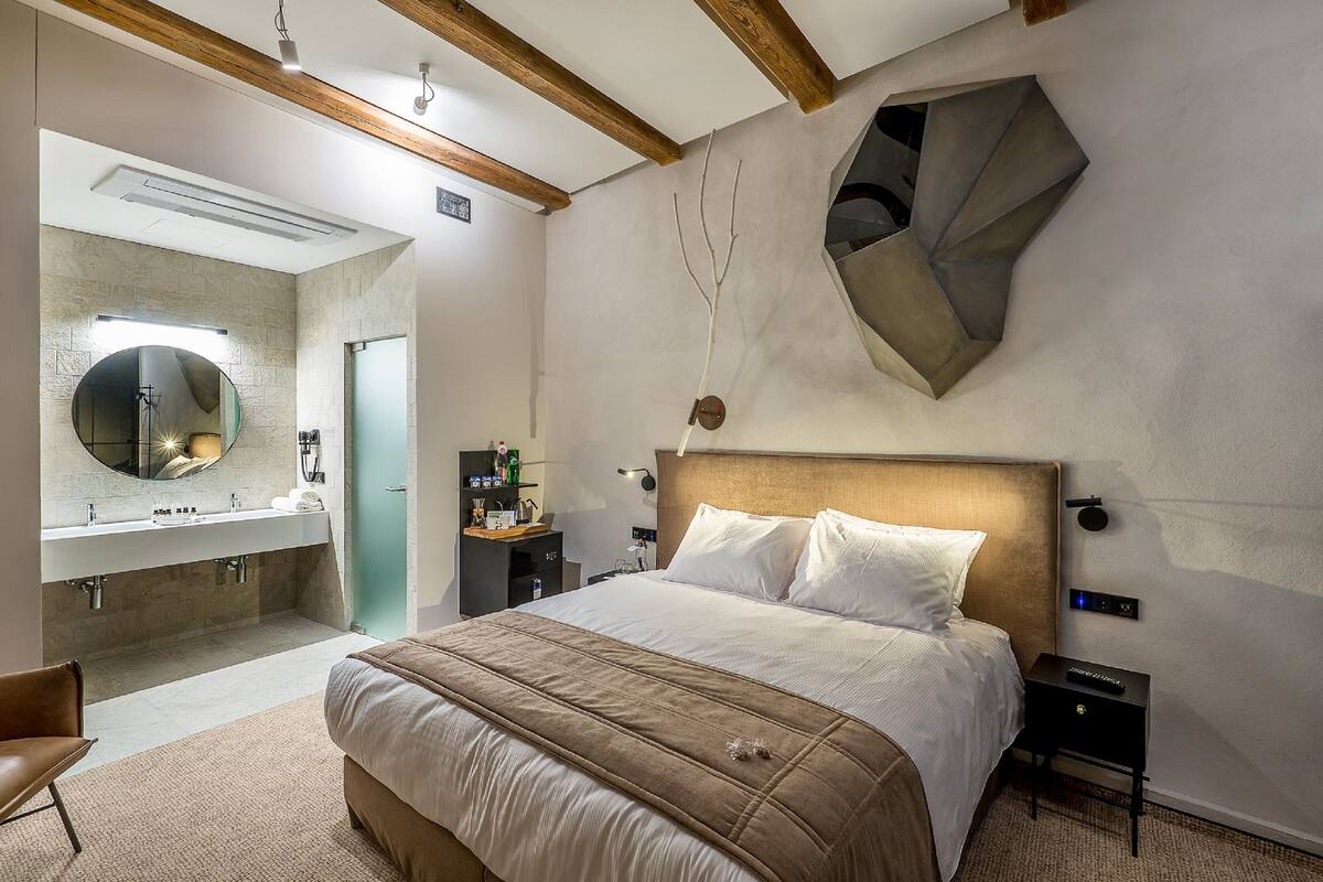A modern hotel room with a large bed, a round mirror, a built-in sink, and a unique geometric wall decoration.