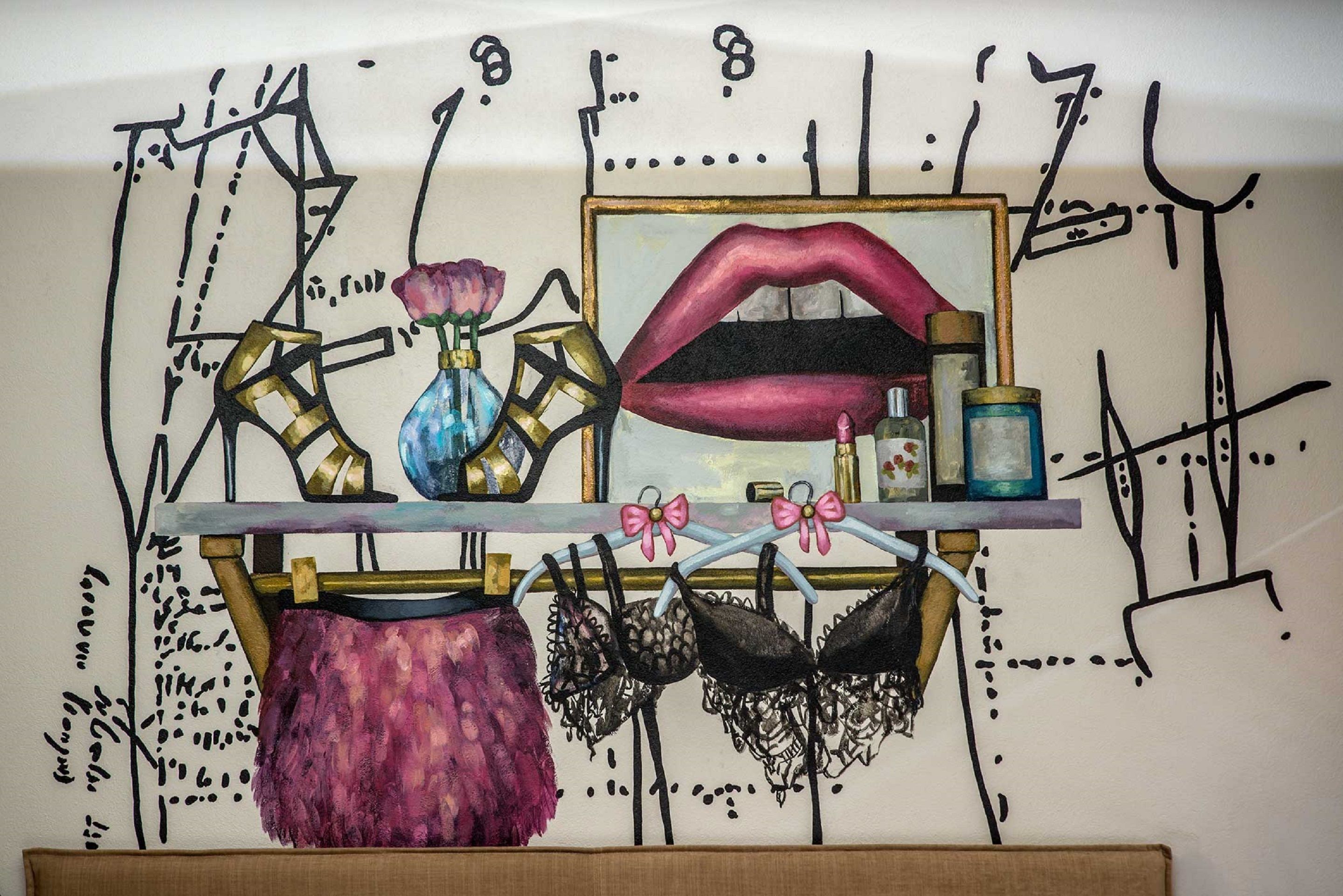 A wall with a mirror, a vase with a flower, a pair of lips, and several bras on a rack.