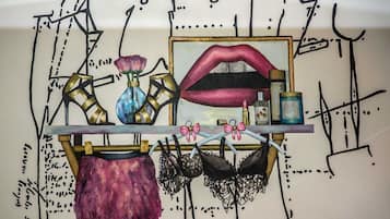 A wall with a mirror, a vase with a flower, a pair of lips, and several bras on a rack.