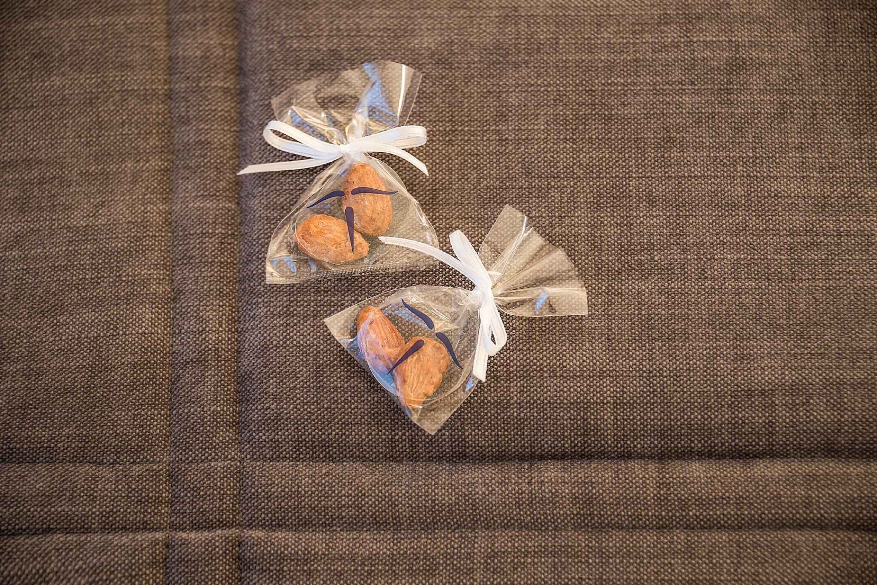 Two small, clear, plastic bags with a brown and blue design, tied with white ribbons, placed on a textured fabric surface.