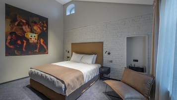 A hotel room with a large bed, a chair, a painting, a brick wall, and a small window.