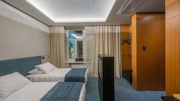 Een hotelkamer met twee bedden, een televisie, een kledingkast en een raam met gordijnen.