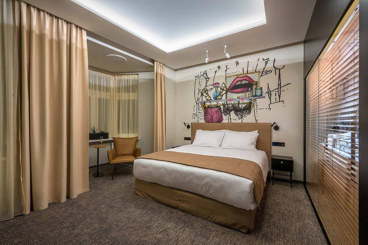 A hotel room with a large bed, a desk, a chair, and a ceiling light.