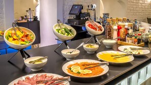 Een buffet met diverse gerechten, waaronder salades, fruit en vlees, gepresenteerd op een toonbank, met een koffieapparaat en andere voorzieningen op de achtergrond.