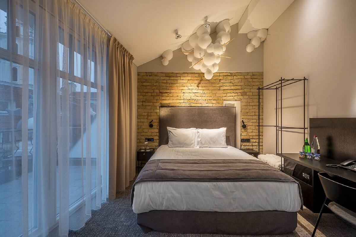 A modern hotel room with a large bed, a desk, and a brick wall.