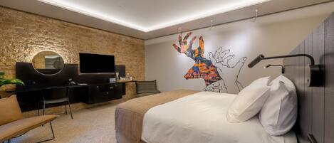 Un dormitorio moderno con una cama grande, un escritorio, un televisor y un mural original en la pared.