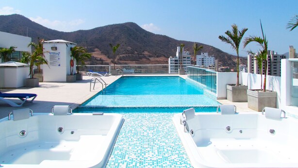 A rooftop pool with clear blue water, surrounded by lounge chairs and potted plants.