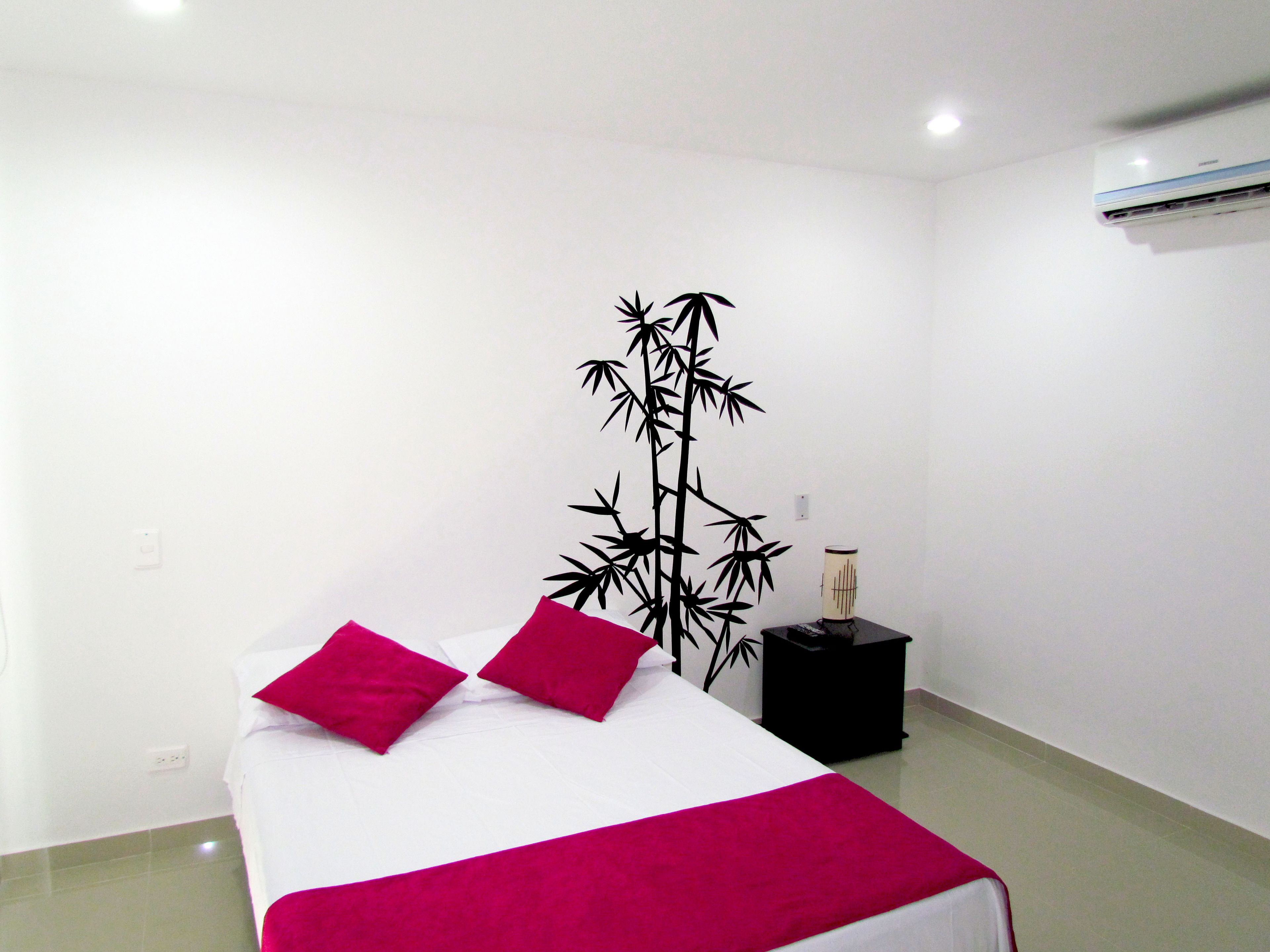 Habitación de hotel con una cama, un adorno decorativo de bambú en la pared, una mesita de noche negra pequeña y un equipo de aire acondicionado blanco.