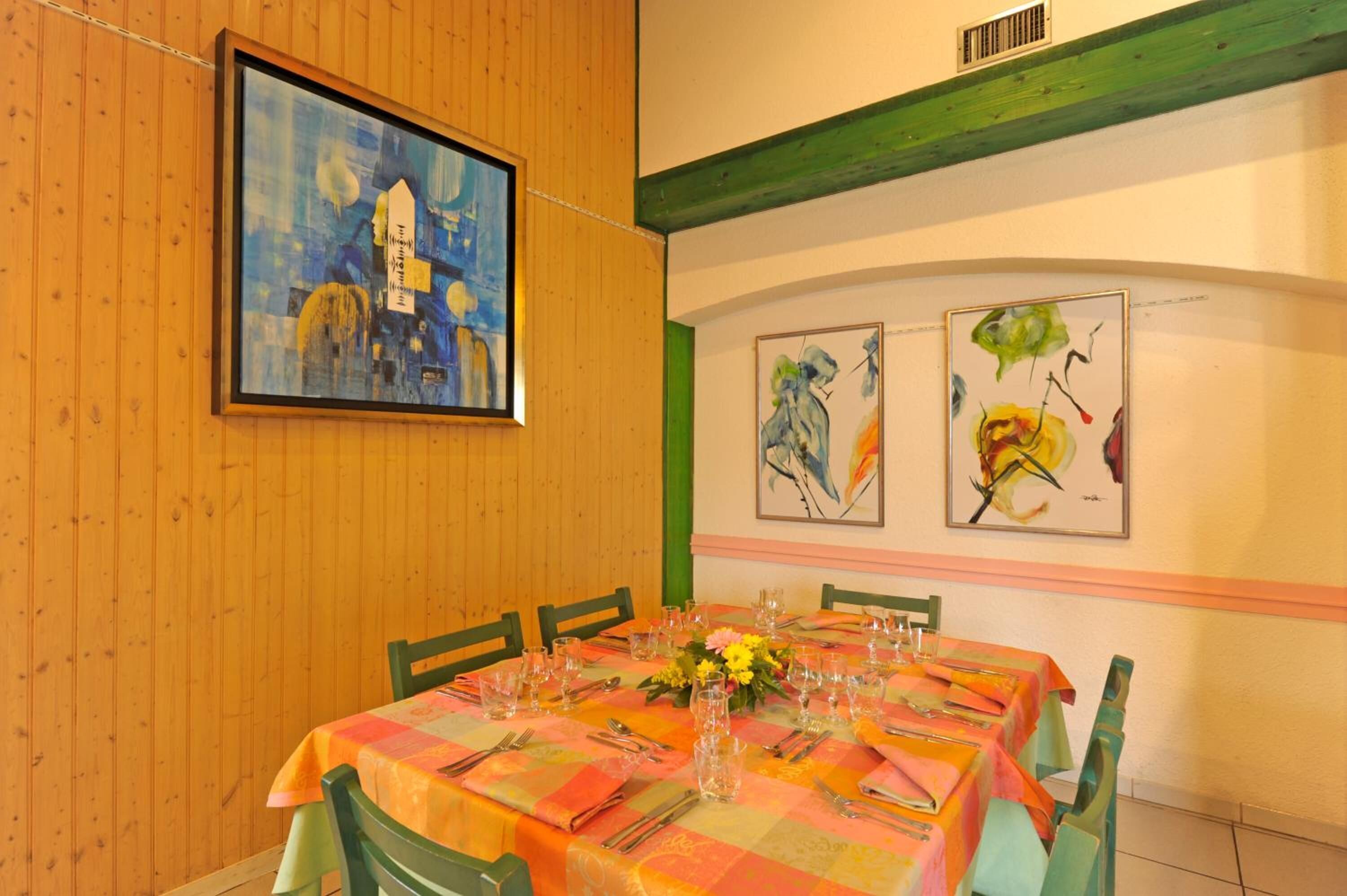 Un comedor con una mesa dispuesta para seis comensales, obras de arte enmarcadas en la pared y paneles de madera.
