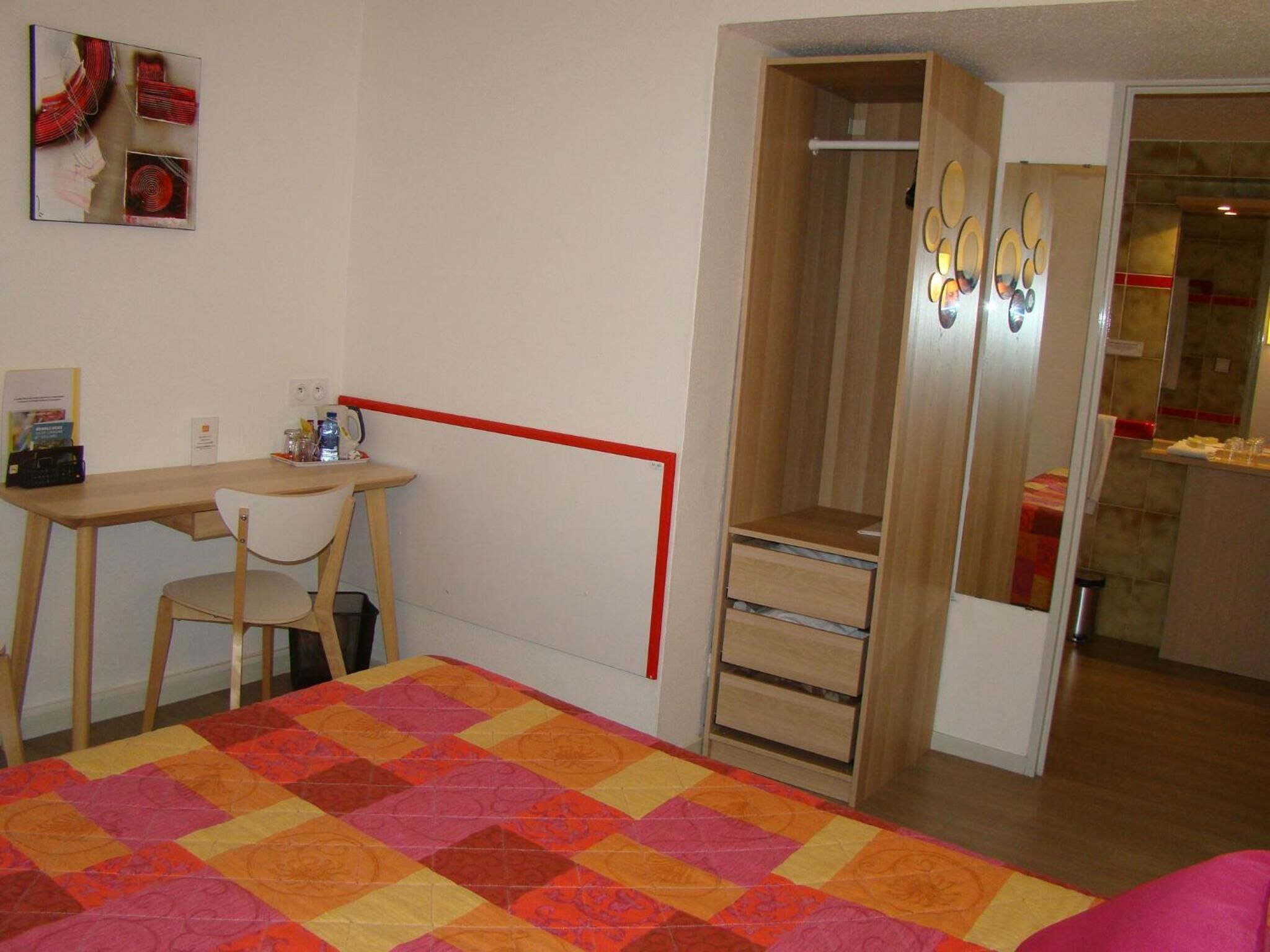 Une chambre à coucher comprenant un lit, un bureau, une chaise, une armoire et un miroir.