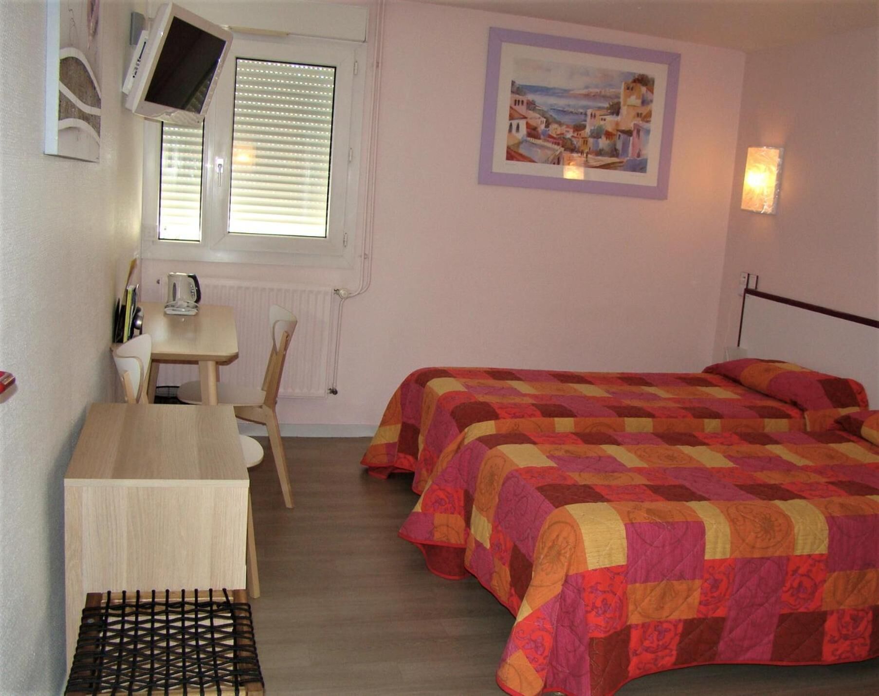 Un dormitorio con dos camas, un escritorio, una silla, un radiador, un televisor montado en la pared y un cuadro en la pared.