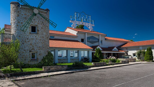 Et hotel med en stenvindmølle, rødt tegltag og et skilt med teksten "Hotel Moulin".