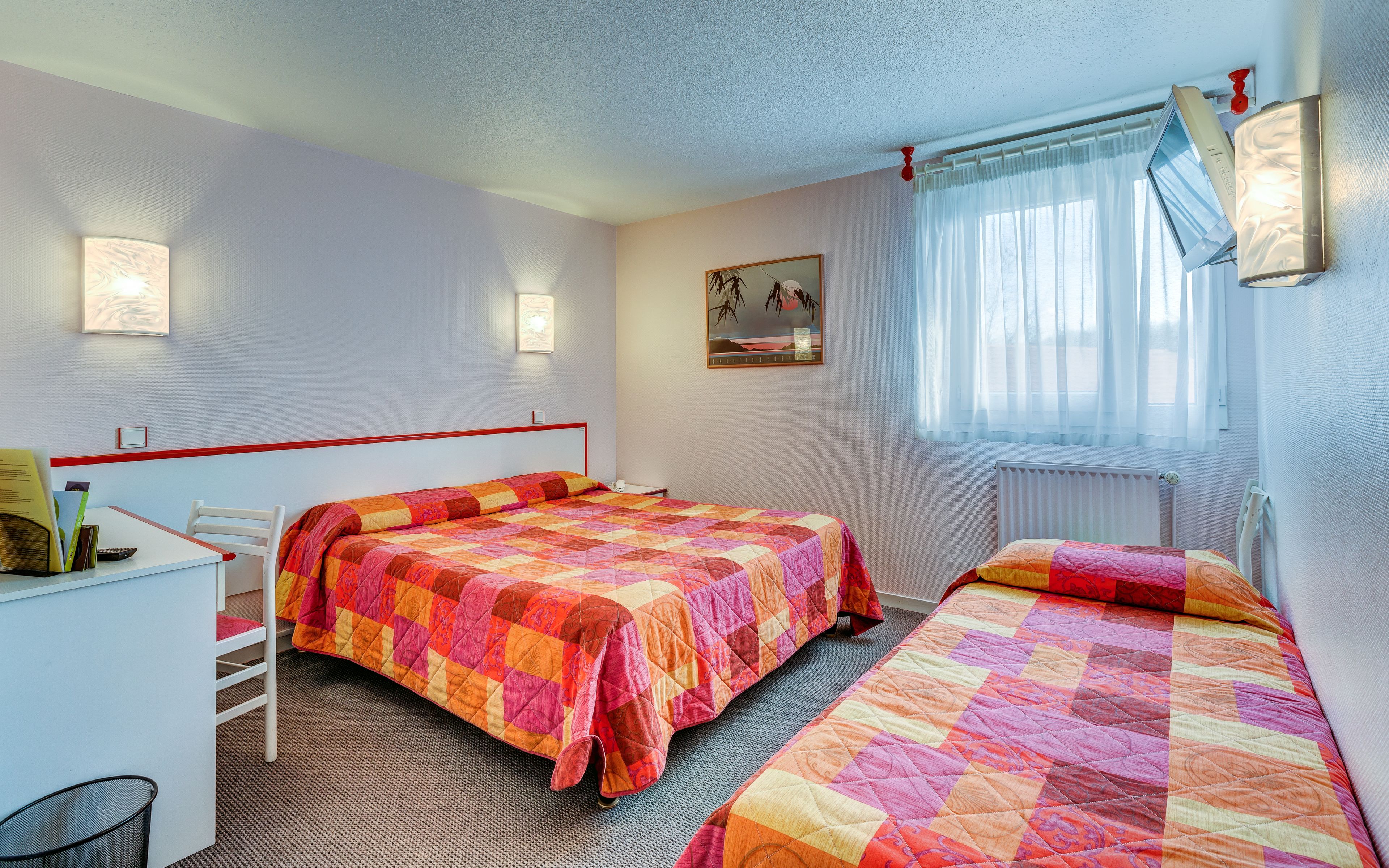 A hotel room with two beds, a desk, and a chair.