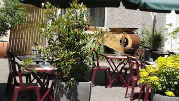 Outdoor seating with tables and chairs, surrounded by potted plants and umbrellas.