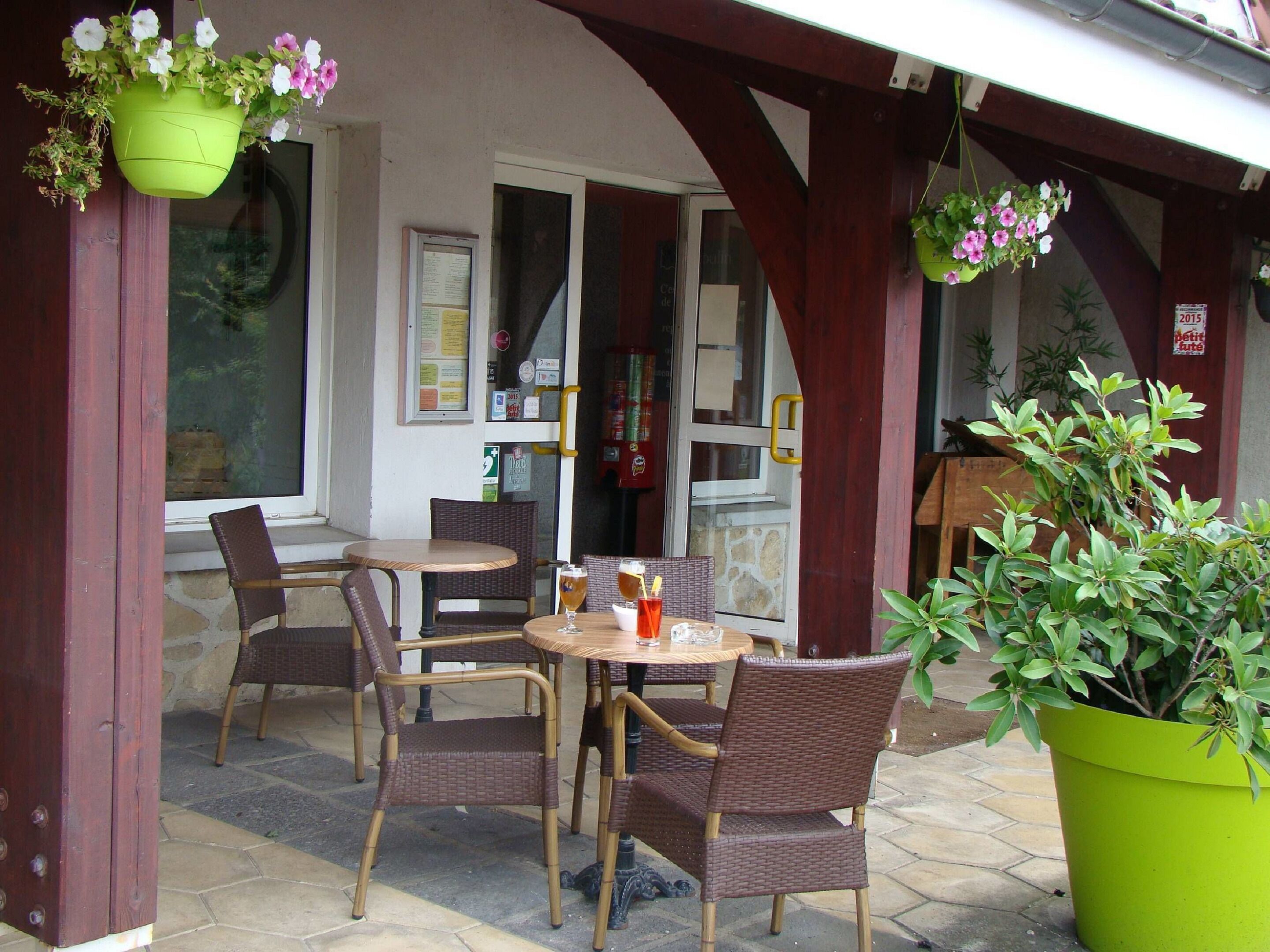 Un patio al aire libre con mobiliario de mimbre, una mesa con una bebida y cestas de flores colgantes.