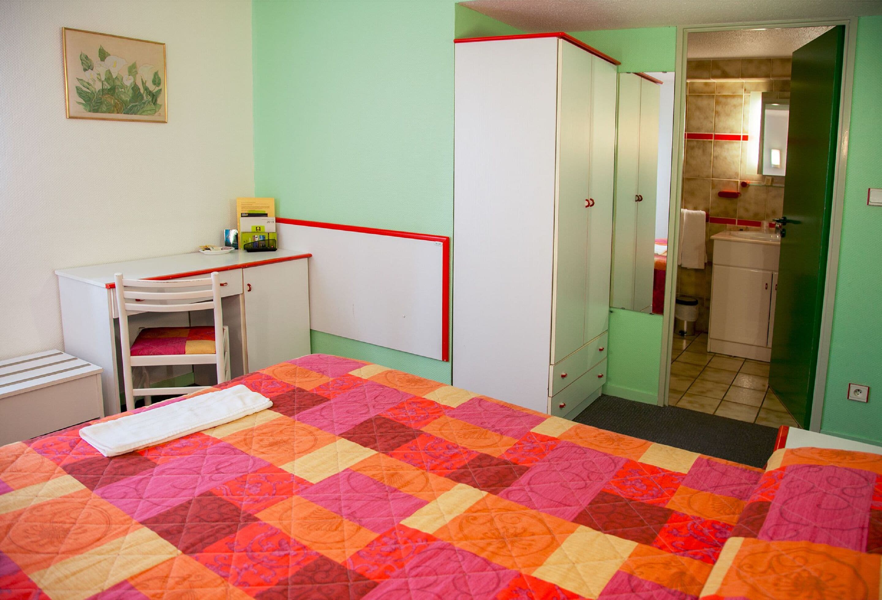 A room with a bed, a desk, a wardrobe, and a bathroom visible through an open door.