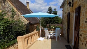 A stone building with a tiled patio, outdoor seating, and a blue umbrella. - Le Jaonnet (Nabirat)