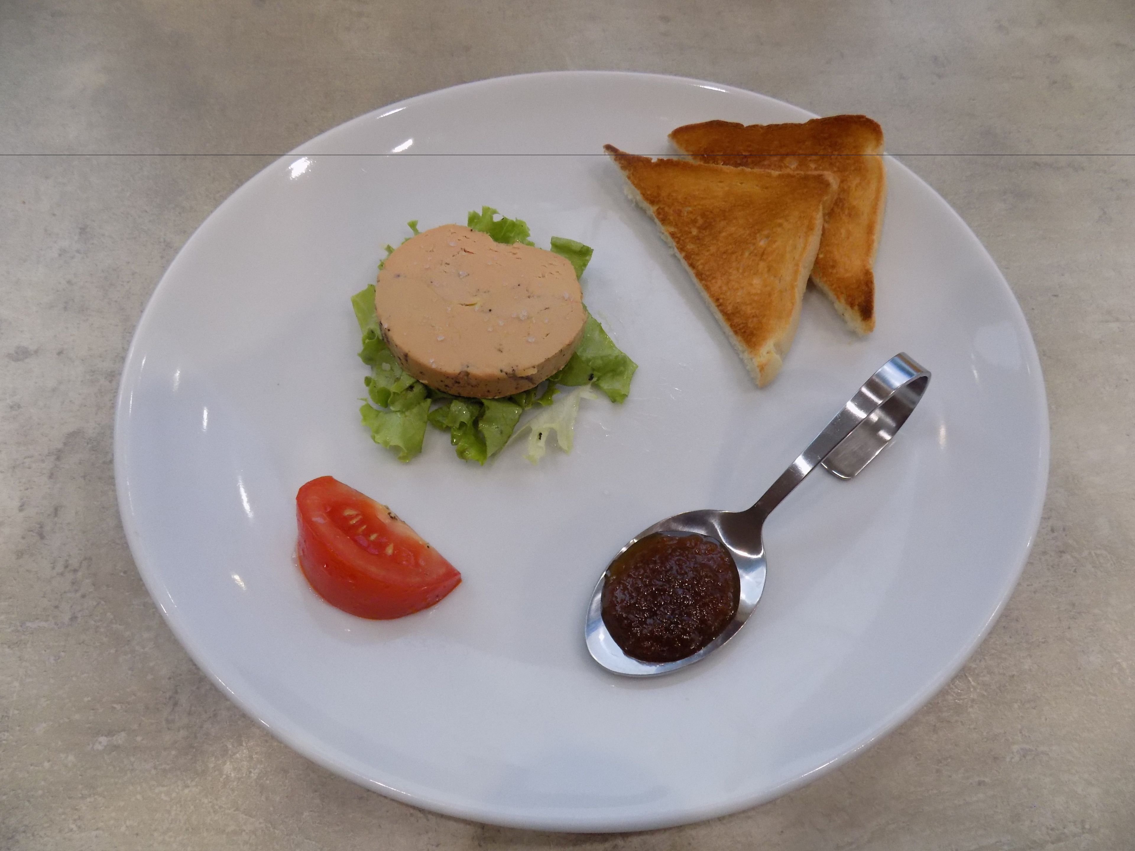 A plate with a sandwich, two slices of toast, a tomato, and a spoon with jam.