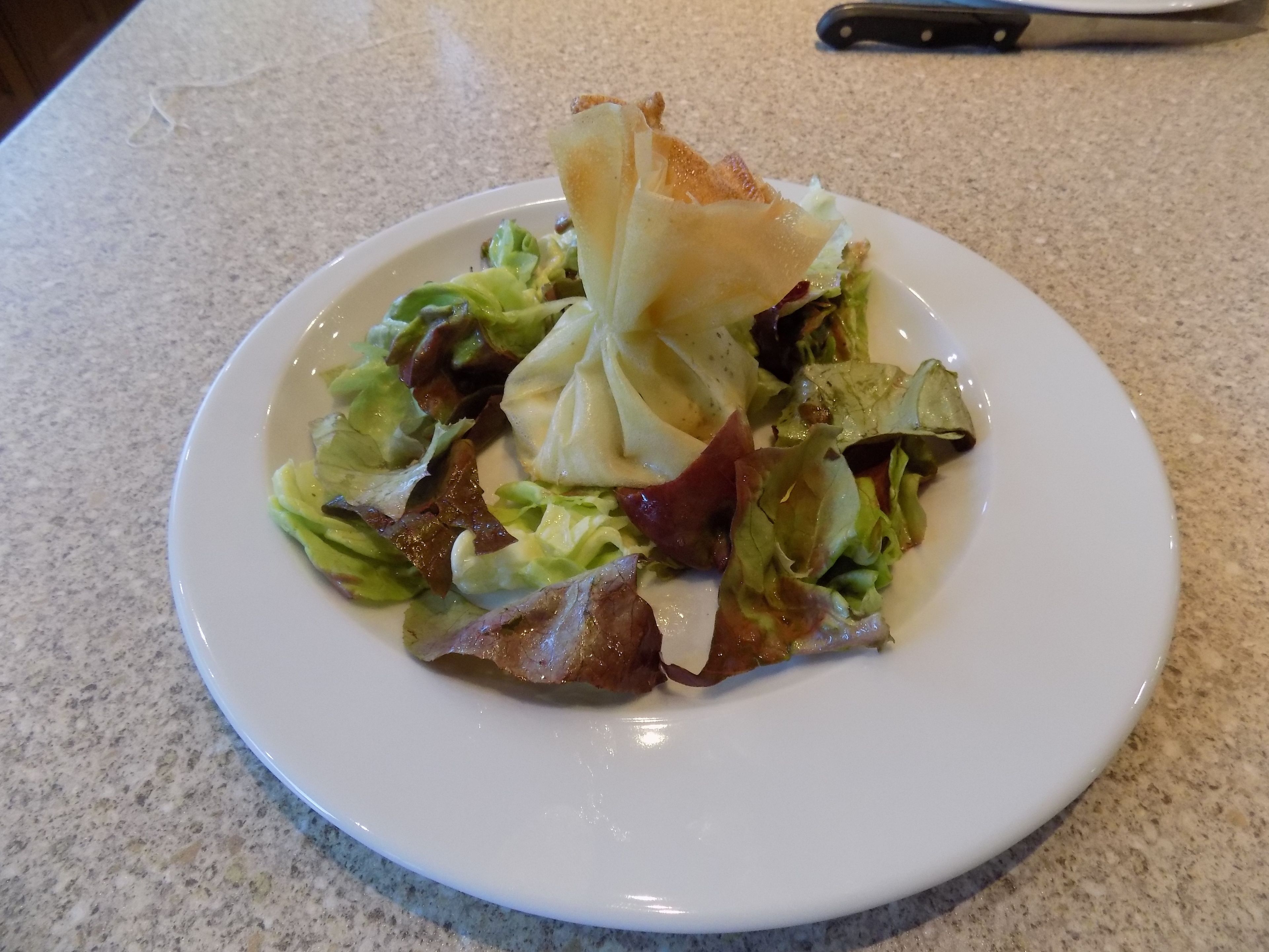 En salatskål med blandede grønne blade og et stykke brød på en hvid tallerken.