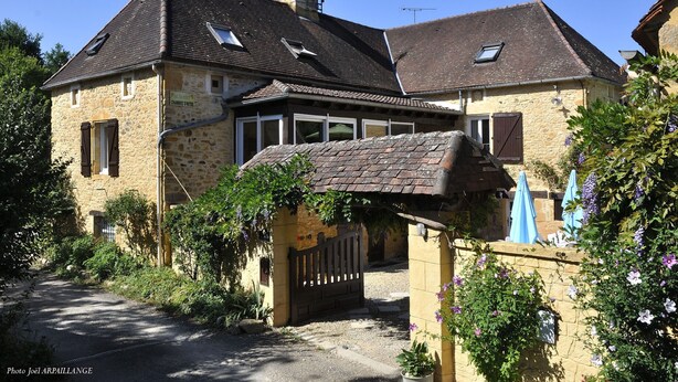 A stone building with a sloped roof, a gated entrance, and a small garden area with potted plants and flowers. - Le Jaonnet (Nabirat)