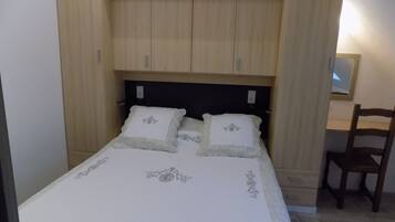 Una camera da letto con un letto, due cuscini, una testiera in legno, una sedia di legno e uno specchio a parete.