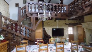 A dining area with a wooden staircase, a chandelier, and a television on the wall. - Le Jaonnet (Nabirat)