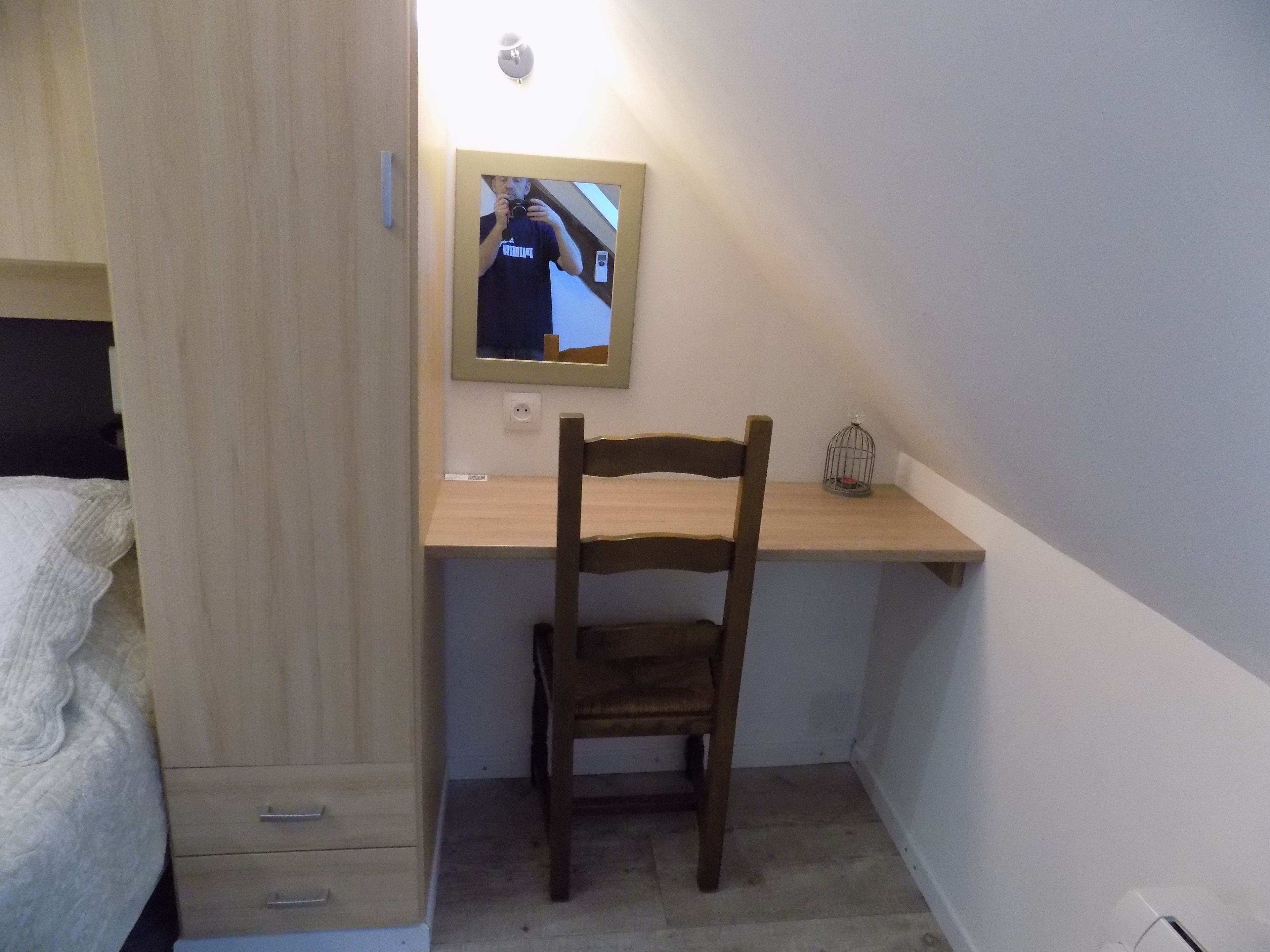 A bedroom with a wooden desk, a chair, a mirror, and a small birdcage.