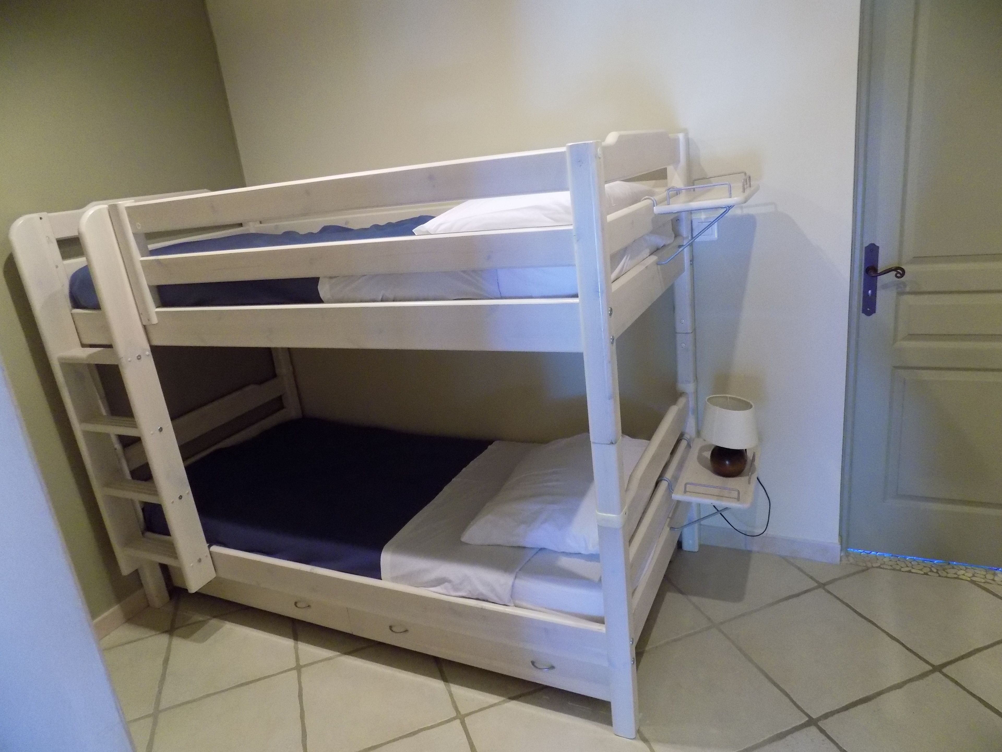 Un lit superposé avec une échelle, une table de chevet avec une tasse, et une porte en arrière-plan.
