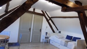 A bedroom with a sloped ceiling, wooden beams, a bed, a chair, a desk, and a wardrobe. - Le Jaonnet (Nabirat)