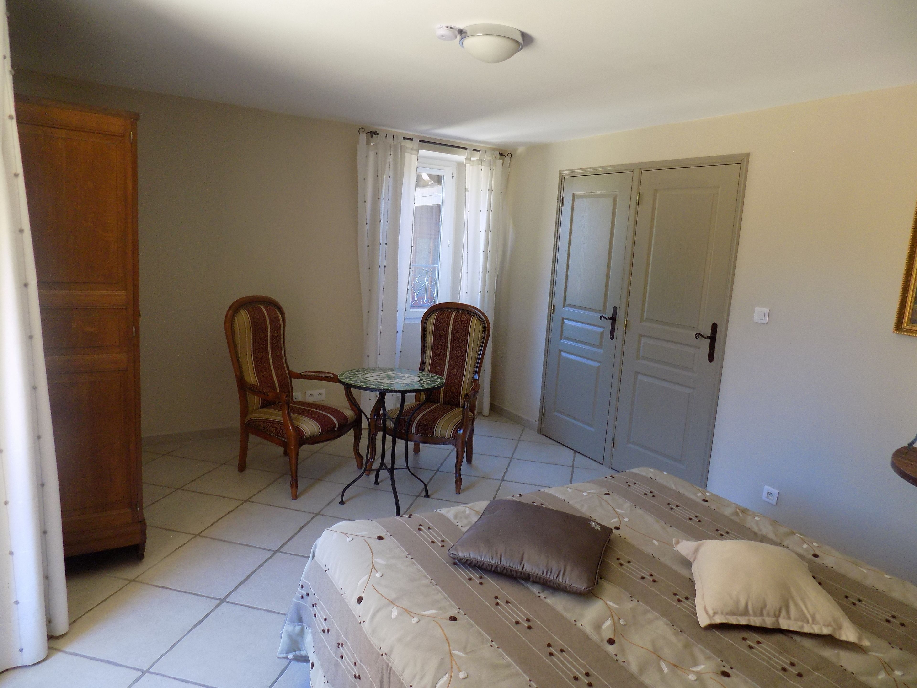 A room with a bed, two chairs, a small table, and a door.