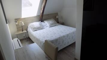 A small, neatly arranged bedroom with a bed, bedside tables, a lamp, and a window.