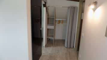 Un pasillo con piso de madera, un armario con barra metálica y una puerta con lámpara.