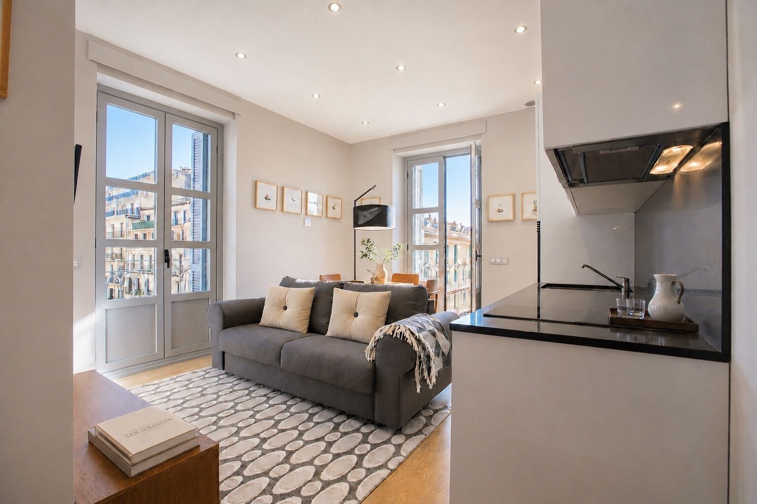 Uma sala de estar moderna com um sofá cinza, uma mesa de centro e uma área de cozinha com fogão e pia.